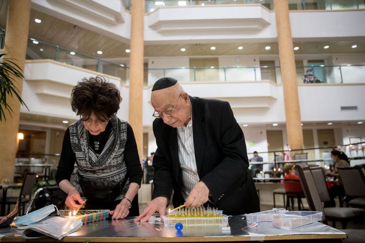 זוג מבוגרים מדליקים נרות חנוכה