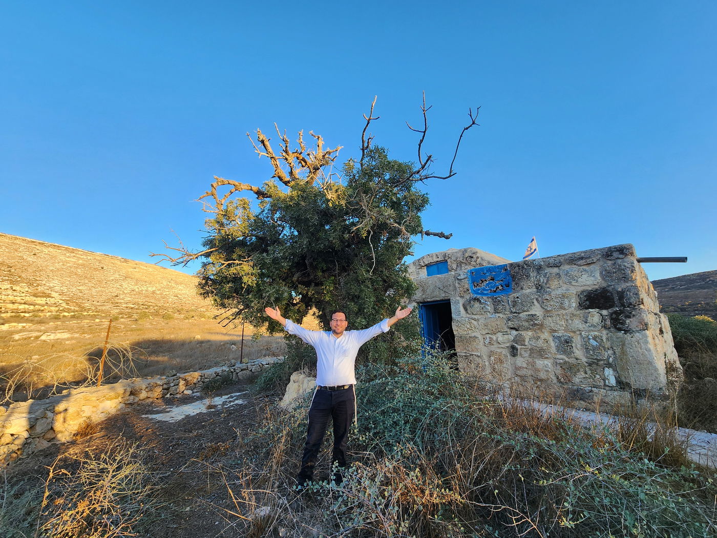 ישראל שפירא לצד האלה העתיקה והמבנה העתיק שהוגדר לאחרונה כקבר אחיה