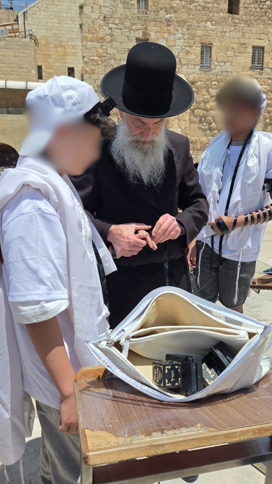הרב אליעזר מנחם ברוידא, שתרם את שמונה זוגות התפילין, כורך את רצועות התפילין על ידי אחד החתנים הניצולים 