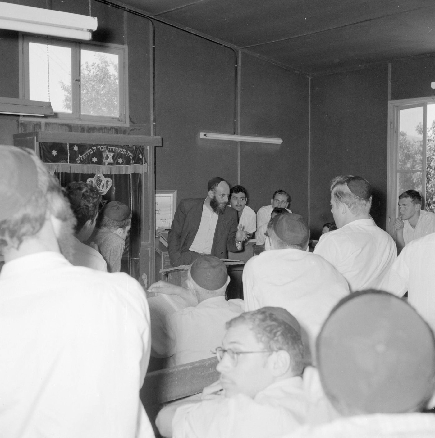 שיעור תוסס בצריף בכפר חסידים: מבטים מרותקים, ספרים פתוחים והתלהבות היסטורית של פעם.